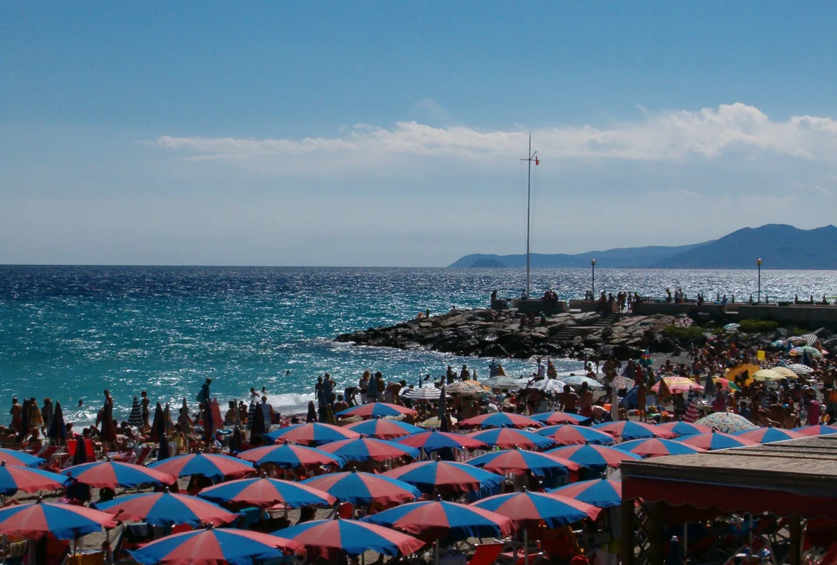 Strand von Finale Pia mit Sonnenschirmen, Badegästen und Felsmole